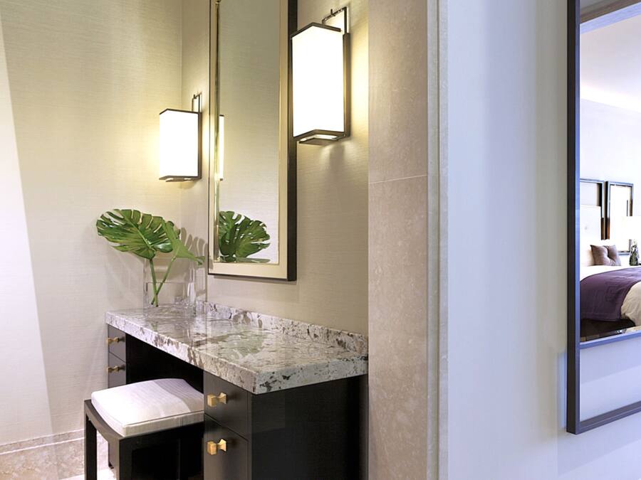 A modern bathroom with a marble vanity, a large mirror, and a bench.