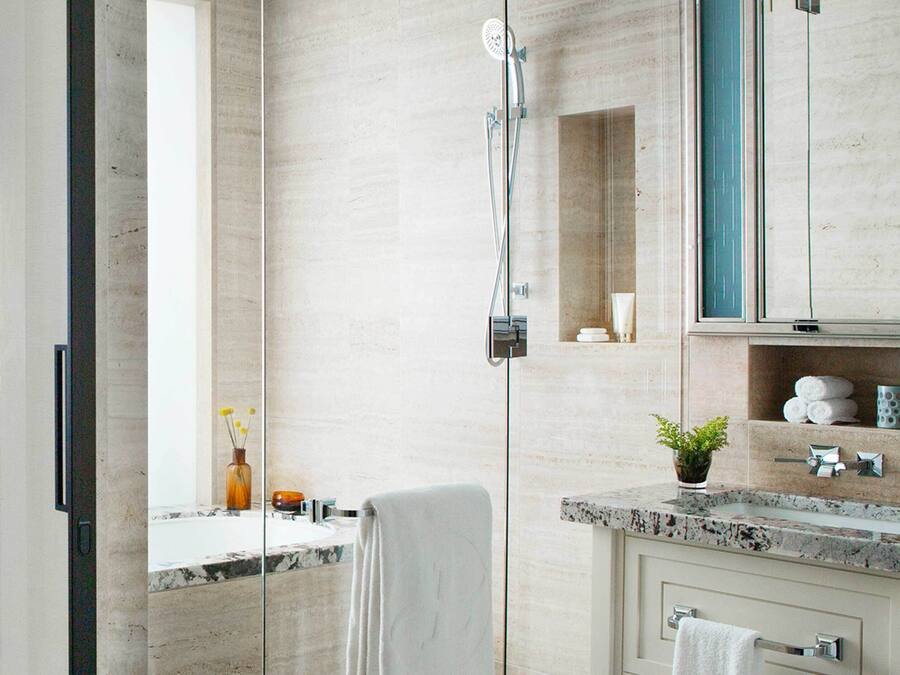 A modern bathroom with a glass shower enclosure, a marble sink, and a built-in cabinet with toiletries.