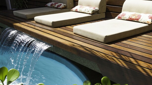 Zona de piscina con sillones de descanso y una pequeña cascada.