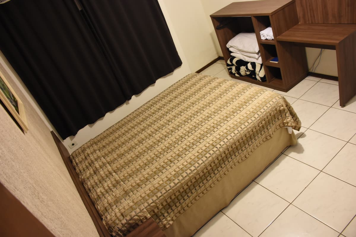 A small, neatly arranged bedroom with a bed, a wooden nightstand, and a shelf with folded clothes.