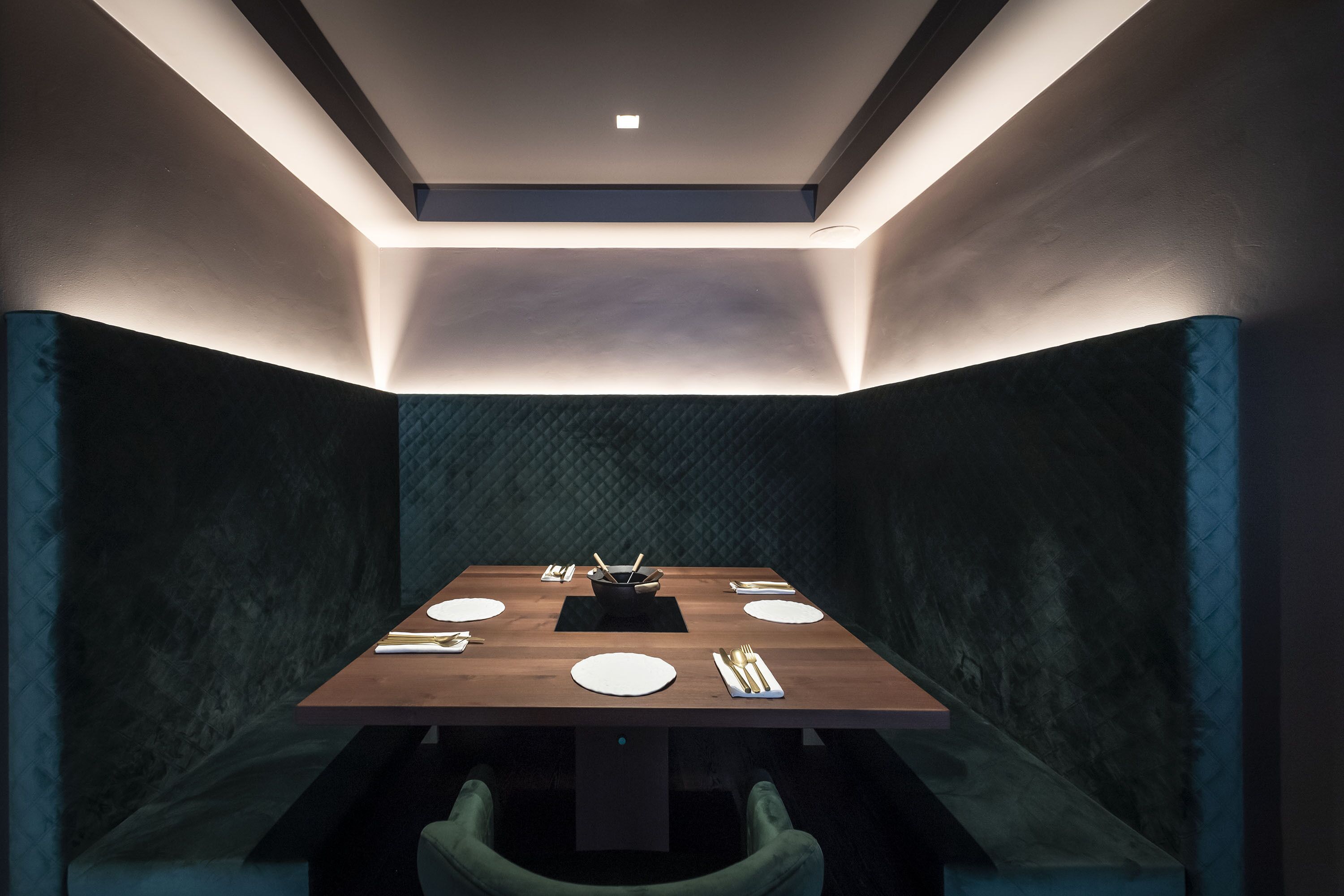 Uma sala de jantar moderna com uma mesa retangular, paredes texturizadas escuras e iluminação embutida no teto.