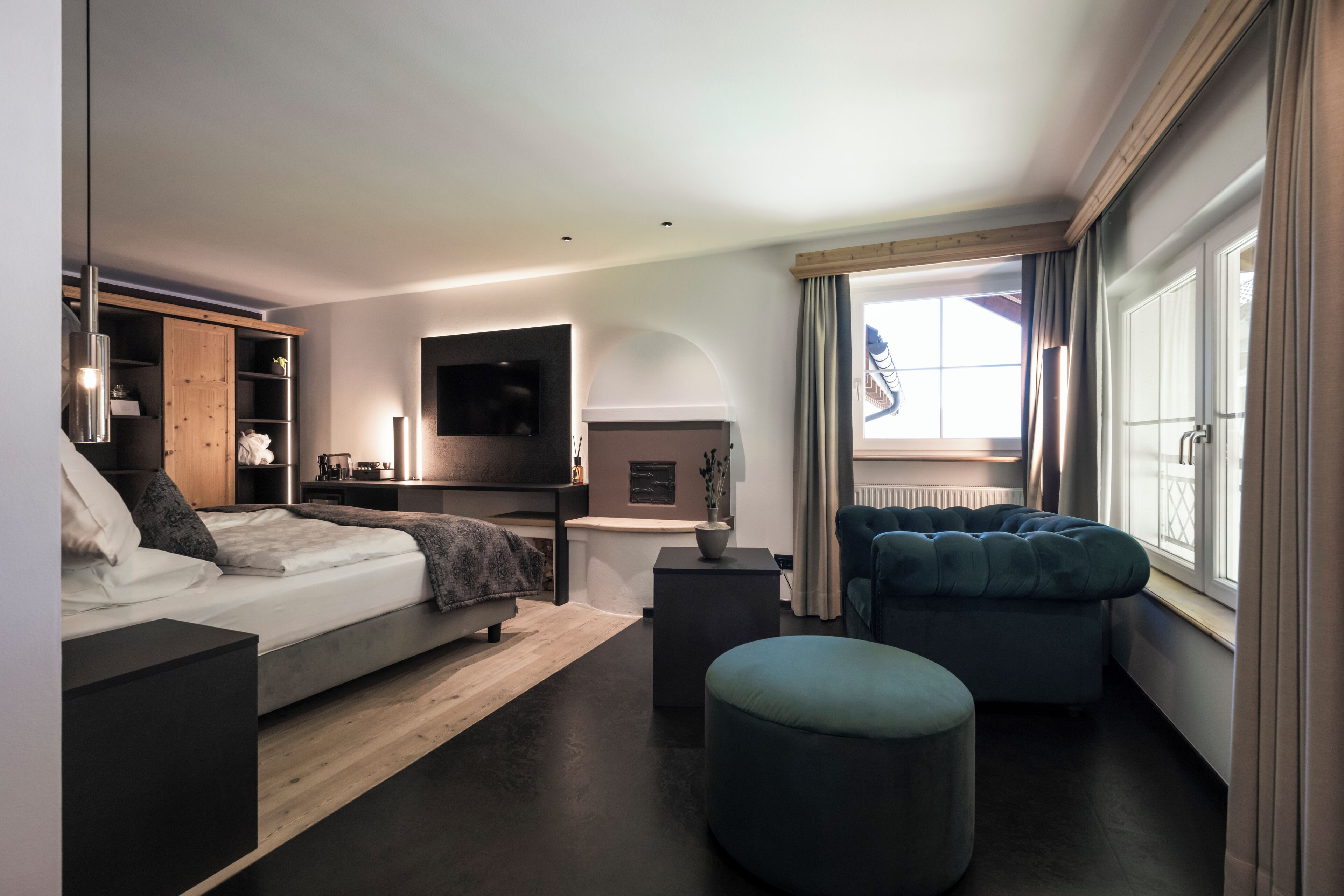 A modern hotel room with a bed, a seating area with a sofa and ottoman, a television mounted on the wall, and a window with curtains.