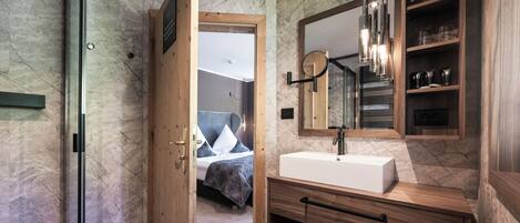 A modern bathroom with a marble wall, a wooden vanity, a large mirror, and a built-in shower.