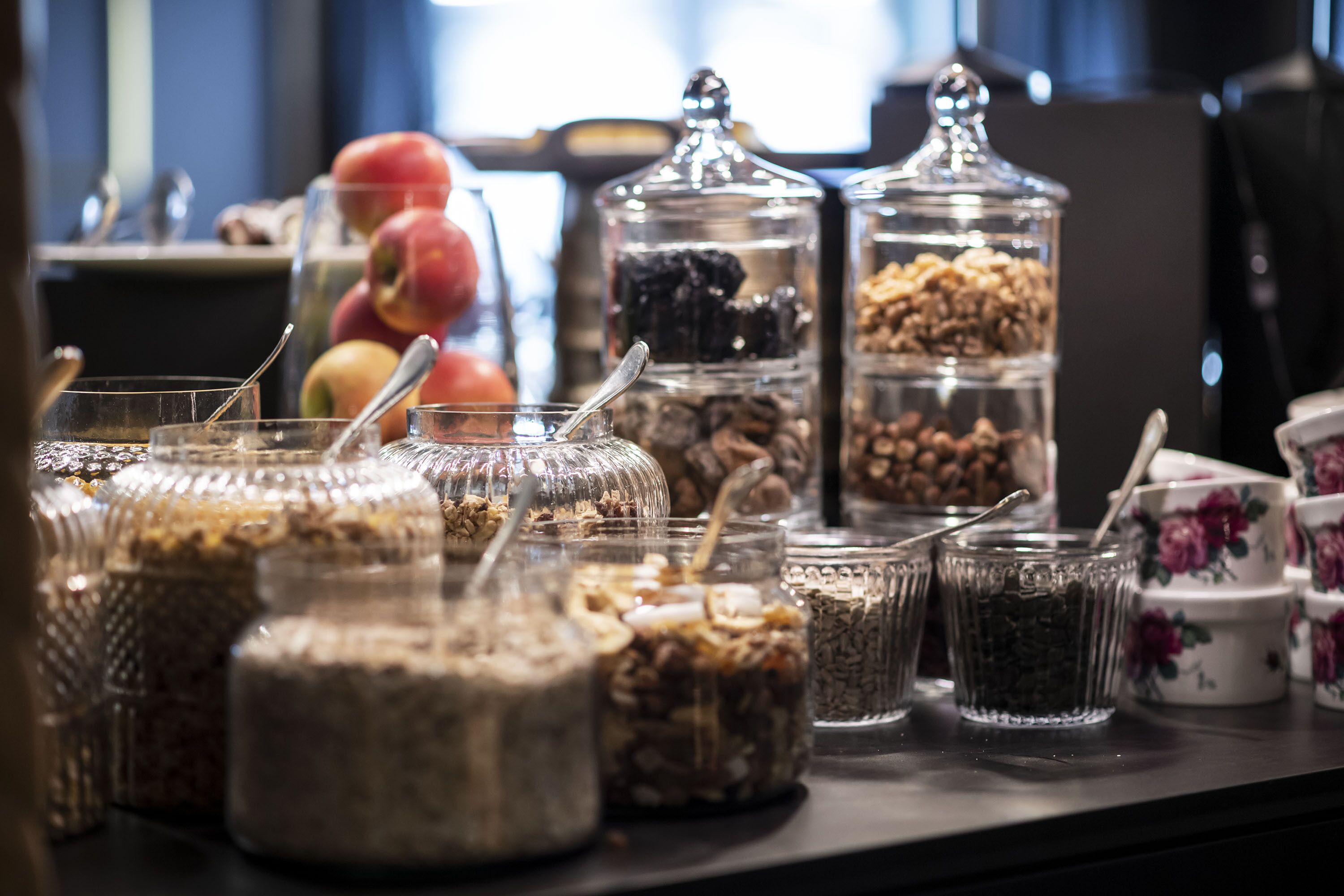 Diversos alimentos en recipientes de vidrio sobre una mesa, como nueces, cereales y frutas secas.
