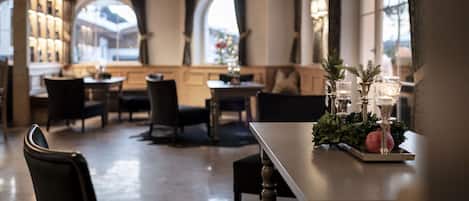 Un comedor con mesas y sillas, un centro de mesa decorativo y ventanas grandes con cortinas.