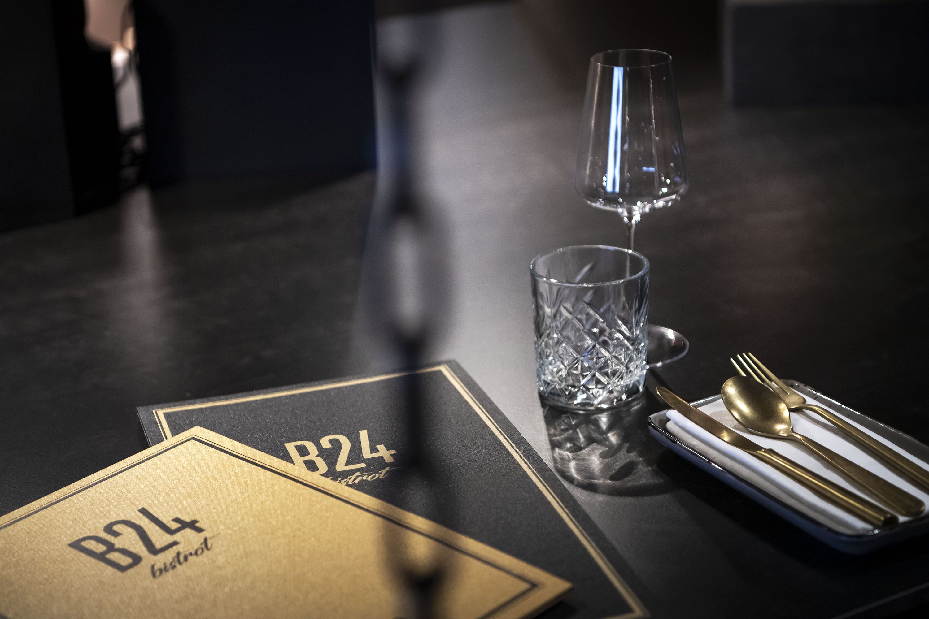 En dækket bord med guld- og sort menu, et glas vand og guldbestik.
