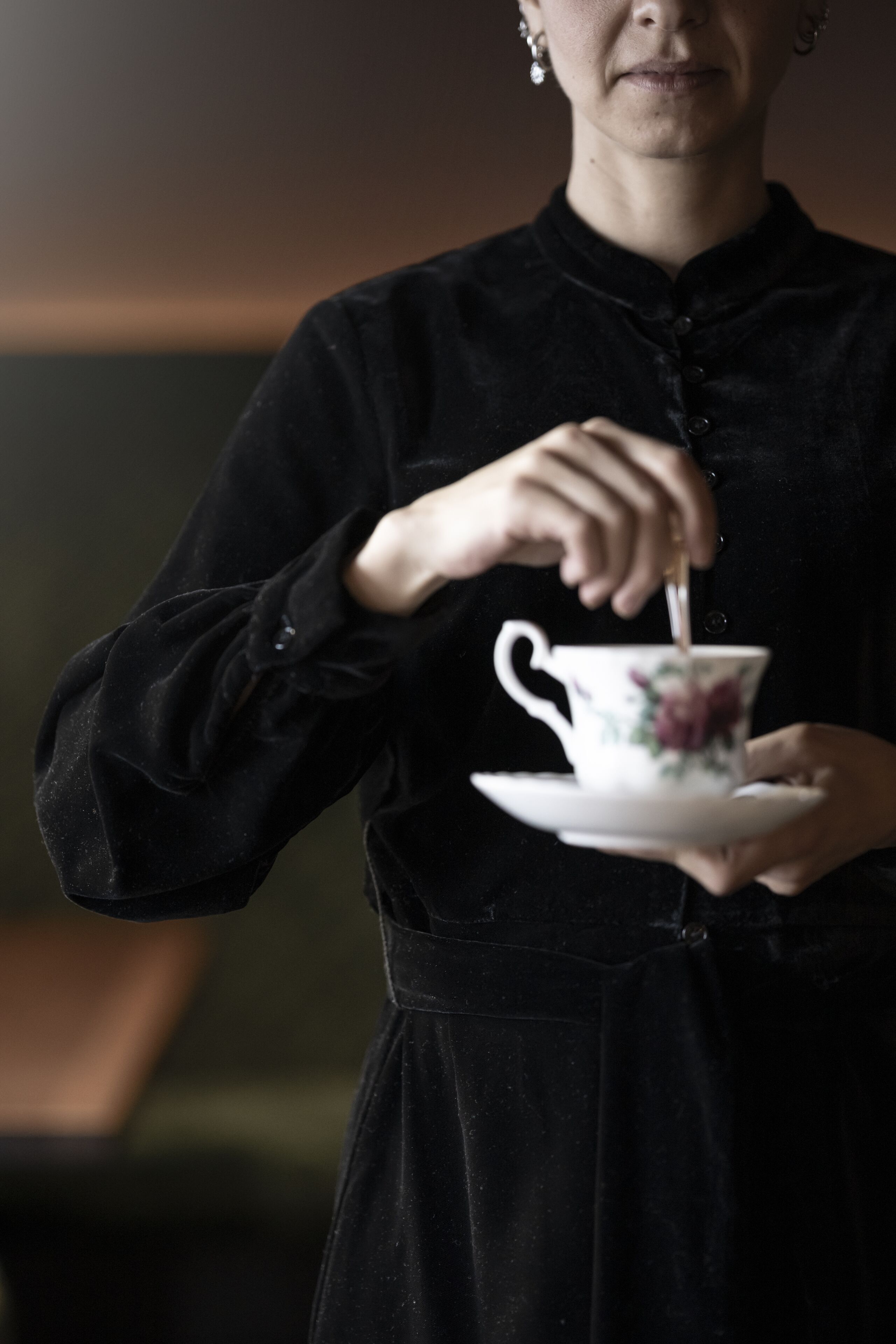 A person in a black dress holding a floral teacup and saucer.