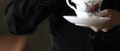 A person in a black dress holding a floral teacup and saucer.
