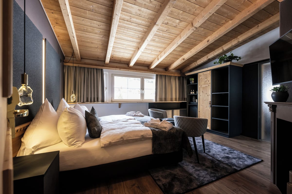 Un dormitorio con techo de madera, una cama con ropa de cama blanca, una silla, un escritorio y una estantería.