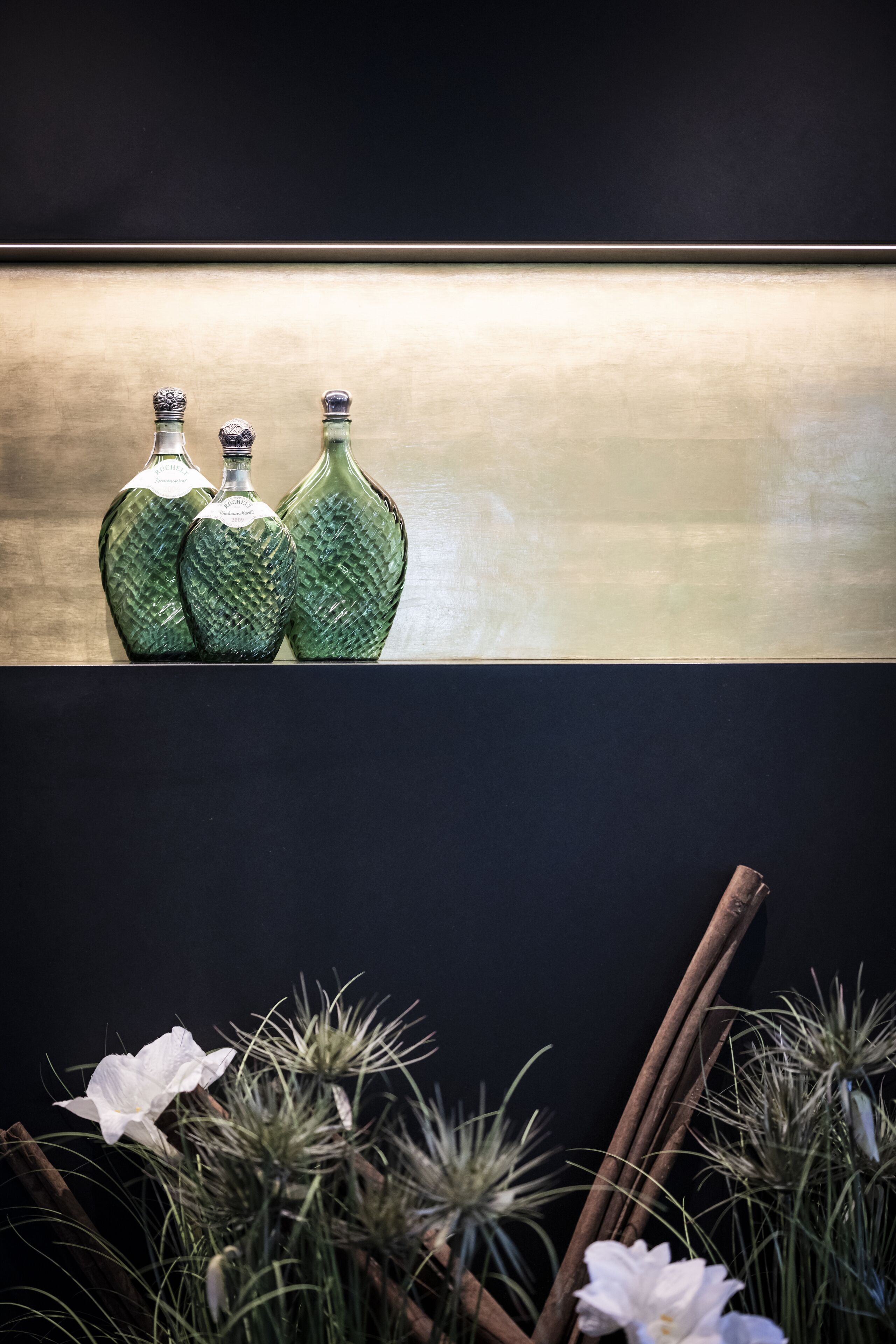 Three green glass bottles on a shelf against a dark background.