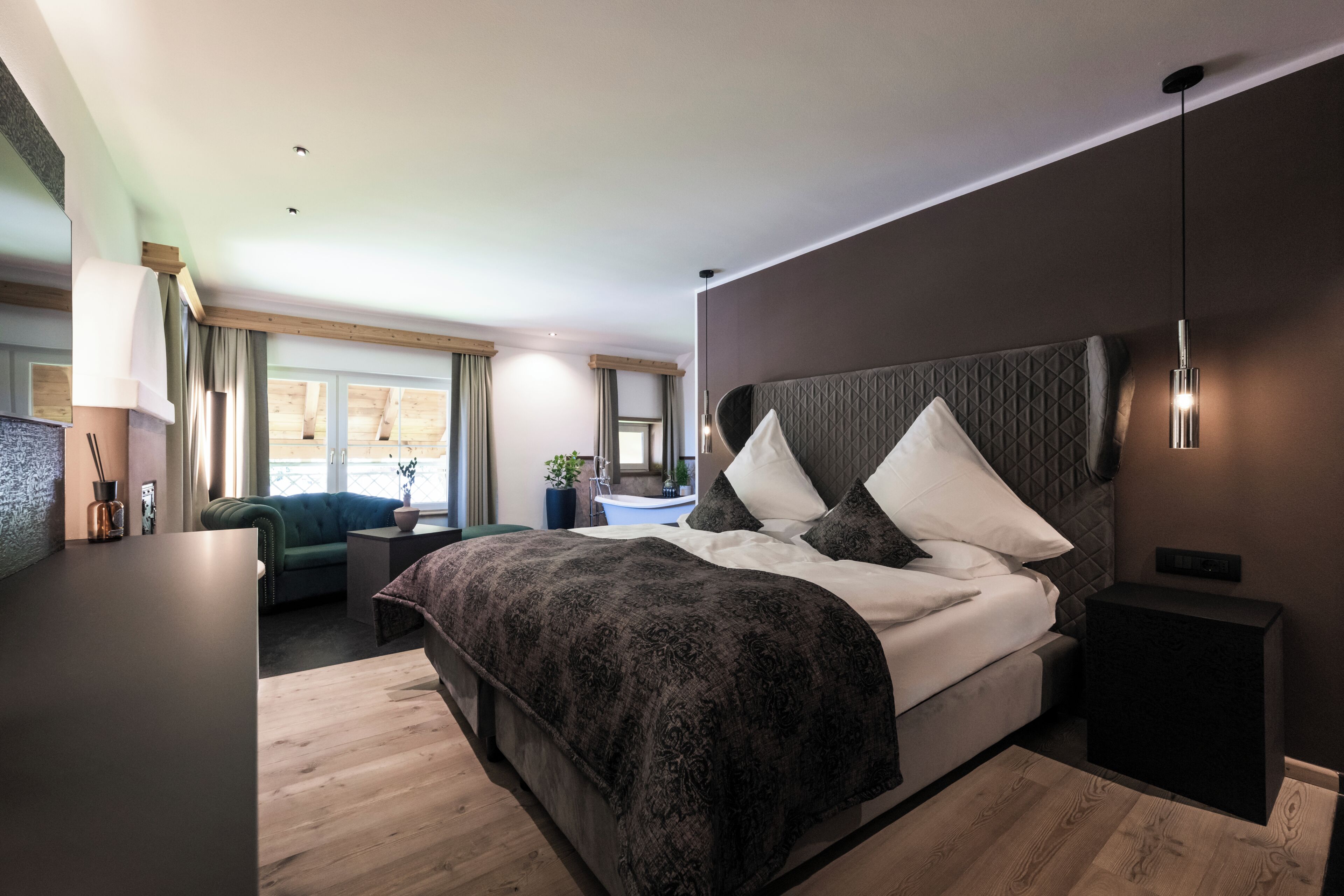 A modern bedroom with a large bed, a bedside table, a nightstand, a desk, and a window with curtains.