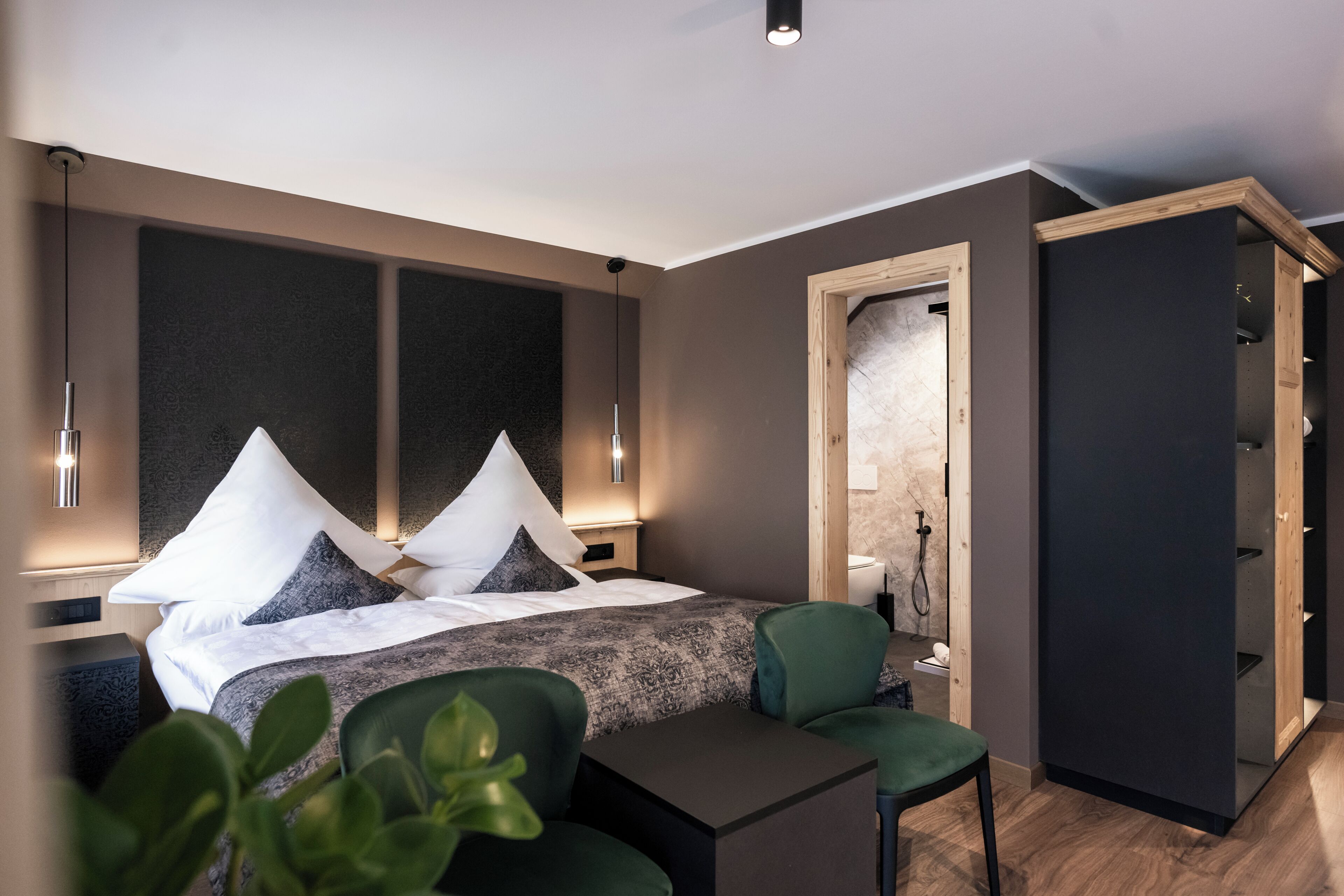 A modern hotel room with a large bed, a small table, a chair, and a walk-in closet.
