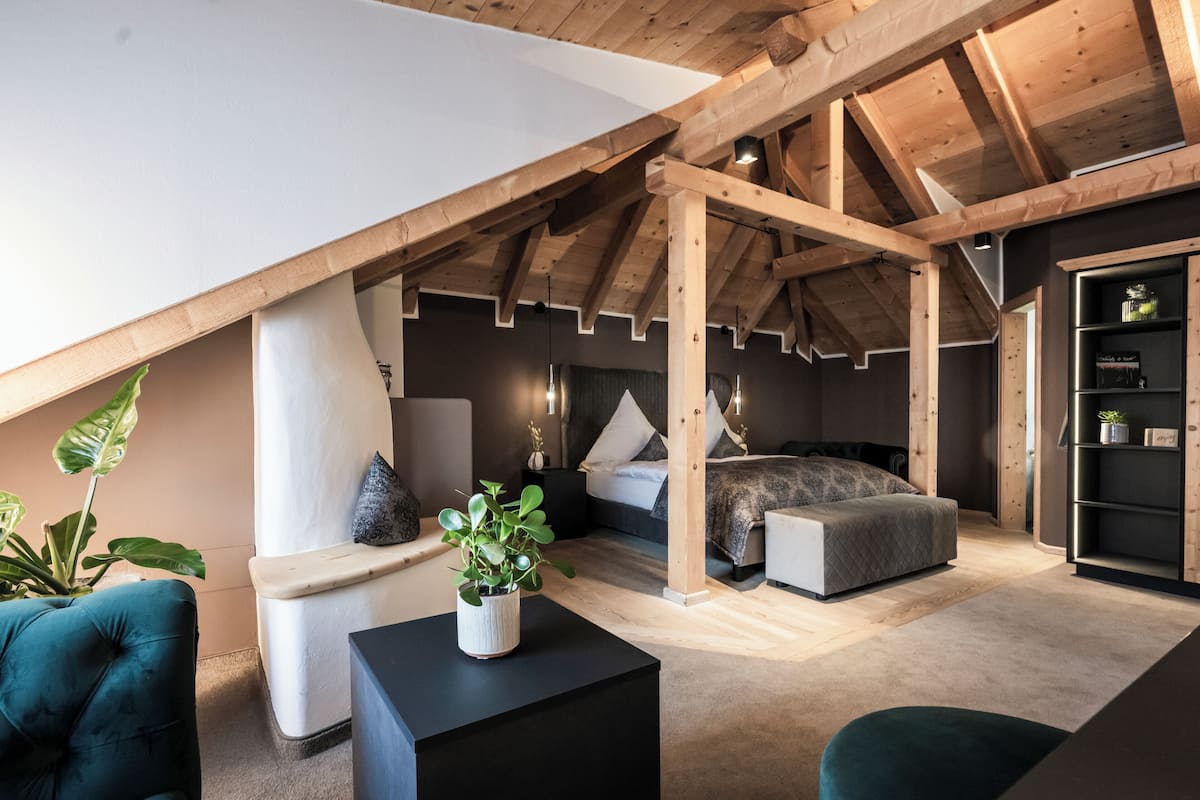 Un dormitorio estilo loft con vigas de madera a la vista, una cama, una zona de estar con una planta y una estantería.