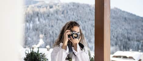 A person taking a photo with a camera, standing in a wooden structure with a snowy mountain in the background.