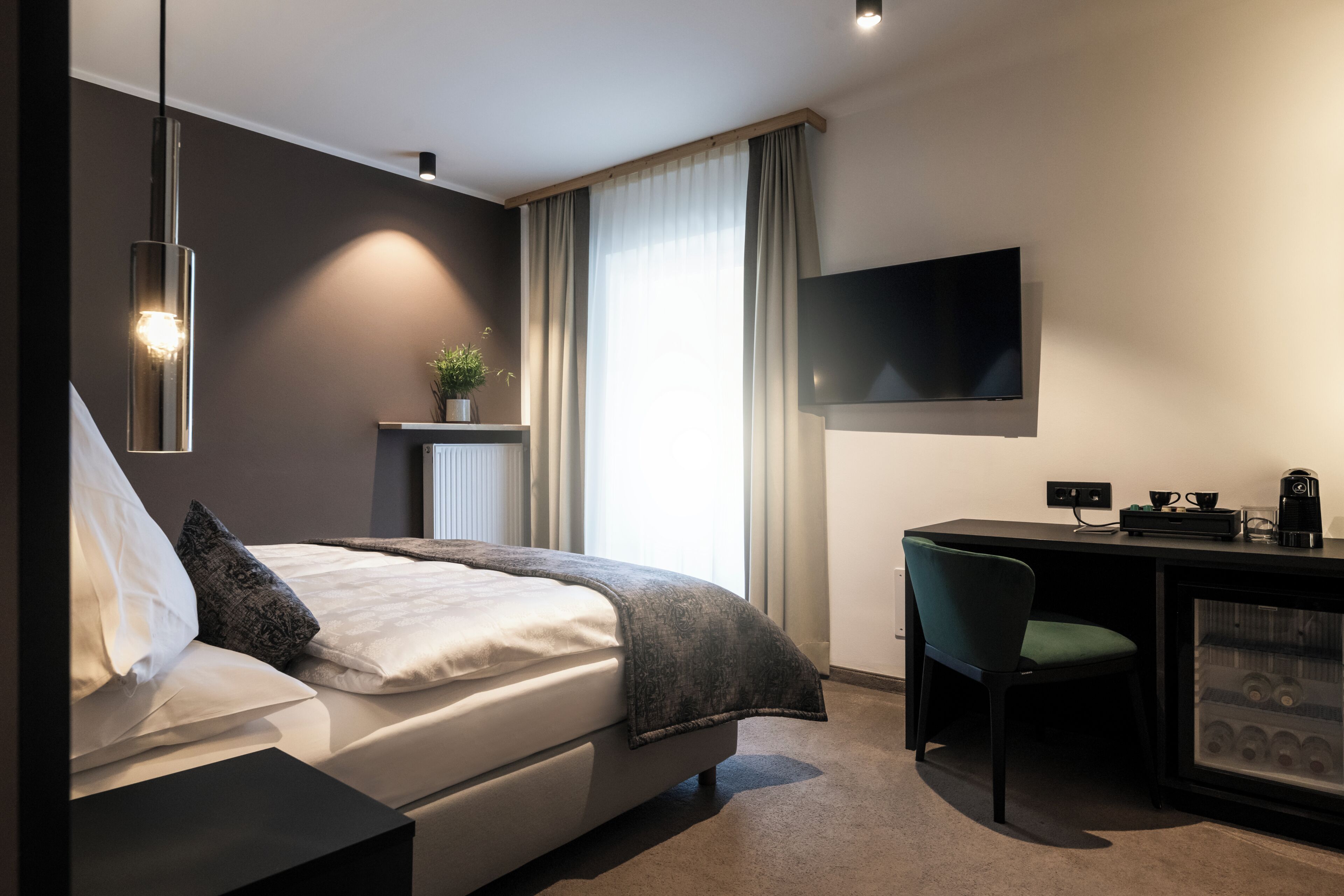 Quarto de hotel moderno com cama, escrivaninha, cadeira, televisão e máquina de café.