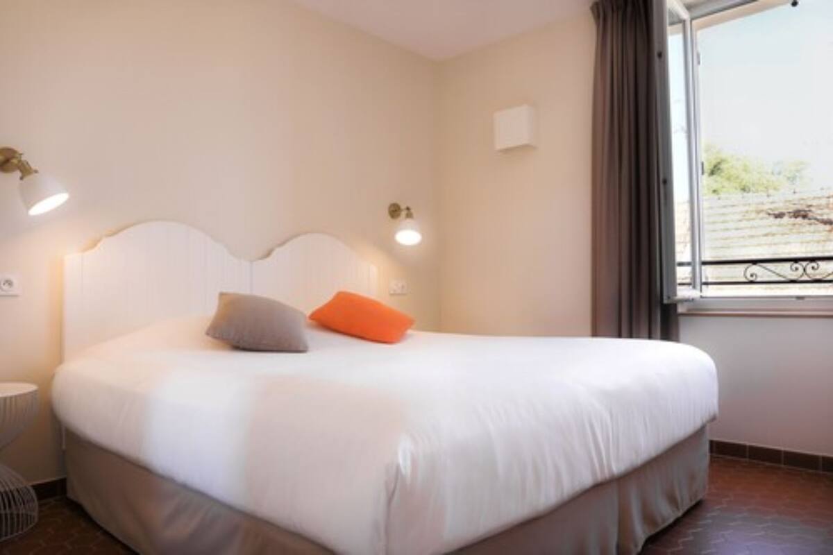Une chambre à coucher avec un lit, une lampe de chevet, une fenêtre avec des rideaux et une vue sur l’extérieur.