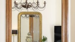 Una habitación con un espejo de marco de madera, una araña, una chimenea y un suelo estampado.