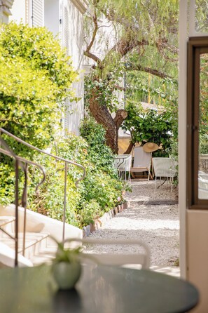 Un cortile con tavolo e sedie, circondato da vegetazione e un albero.