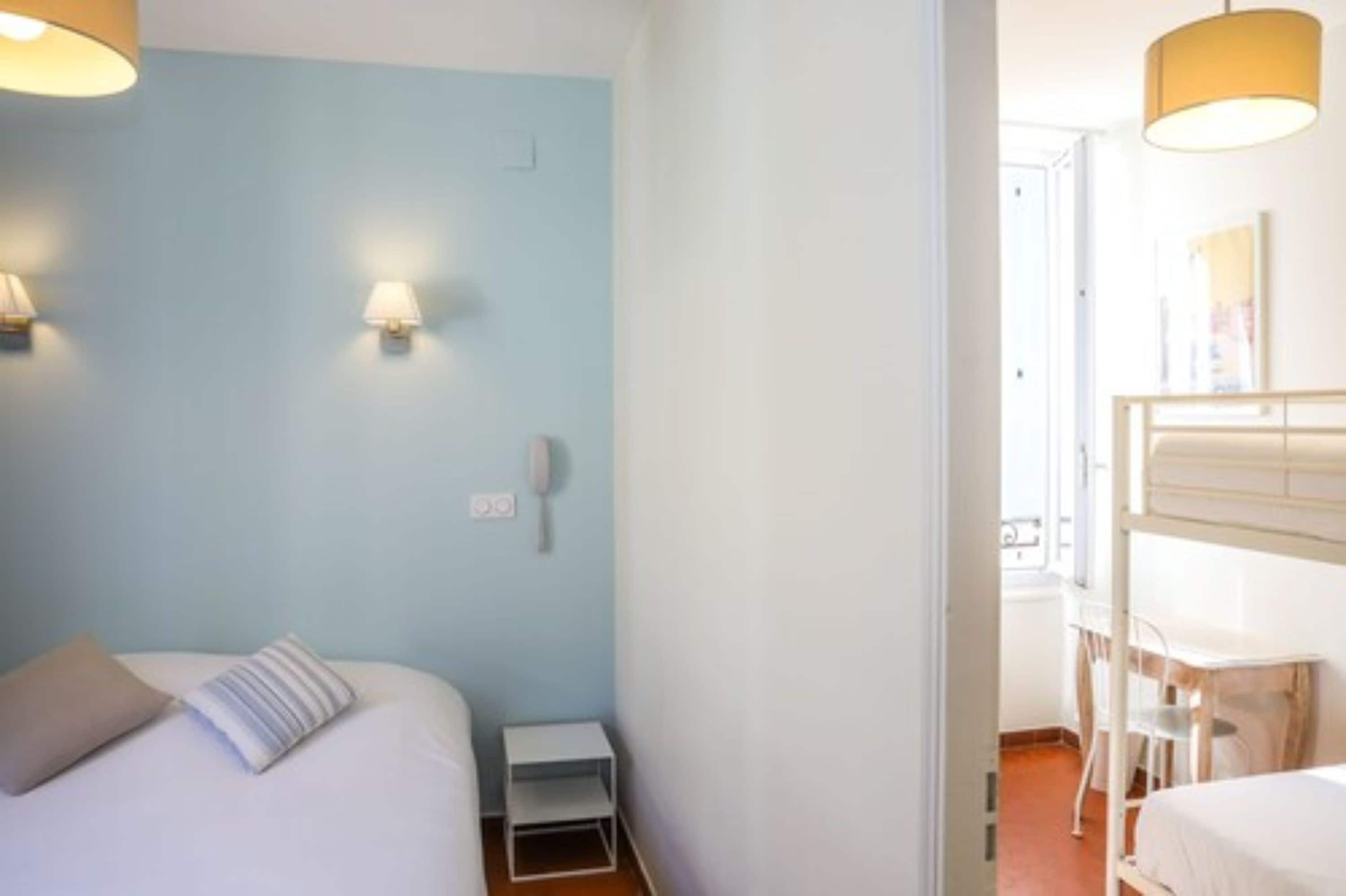 Une chambre d’hôtel comprenant un lit, une table de chevet, une lampe et un petit bureau avec une chaise.