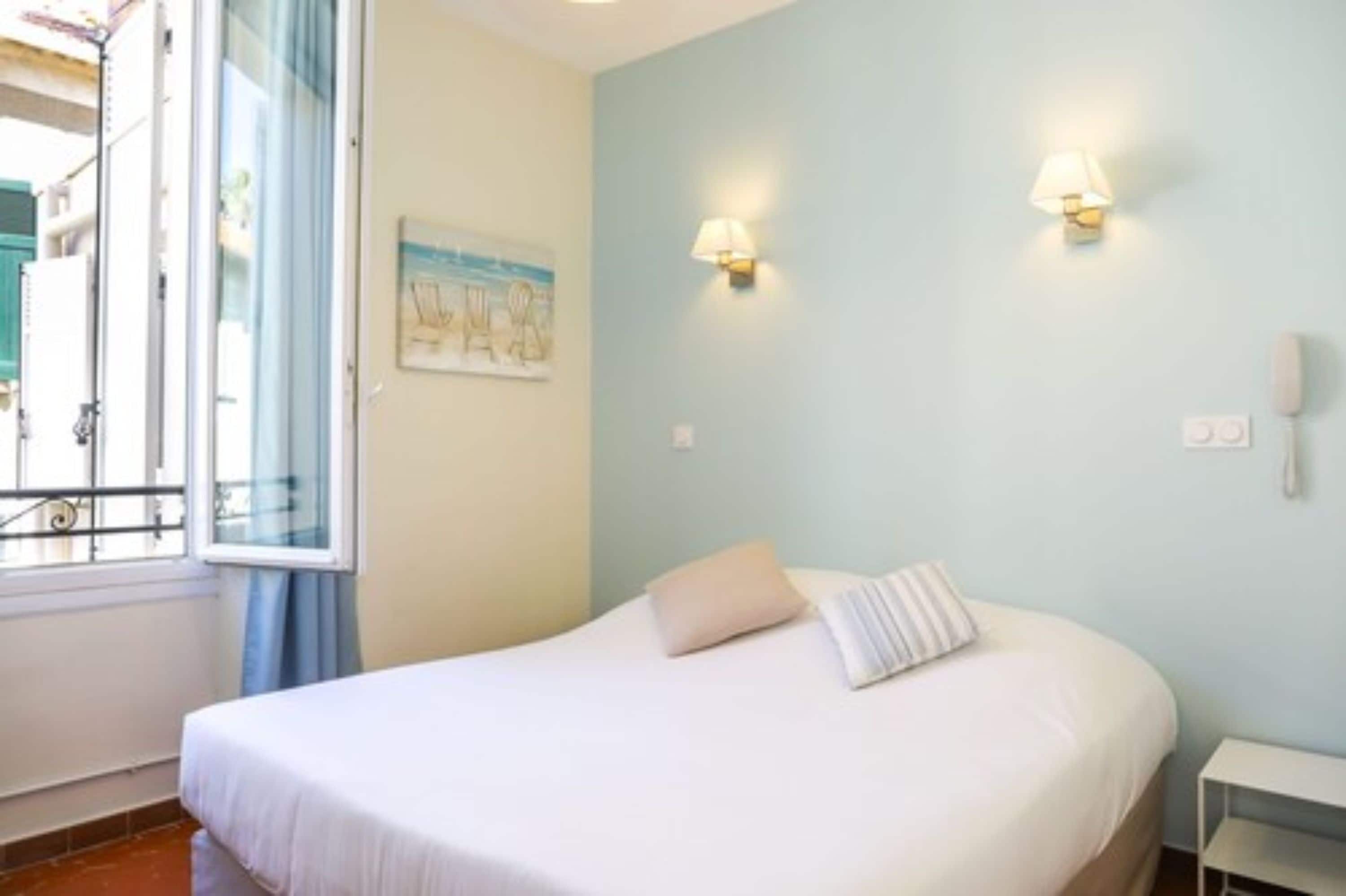 A bedroom with a bed, a nightstand, a wall-mounted lamp, and a painting.