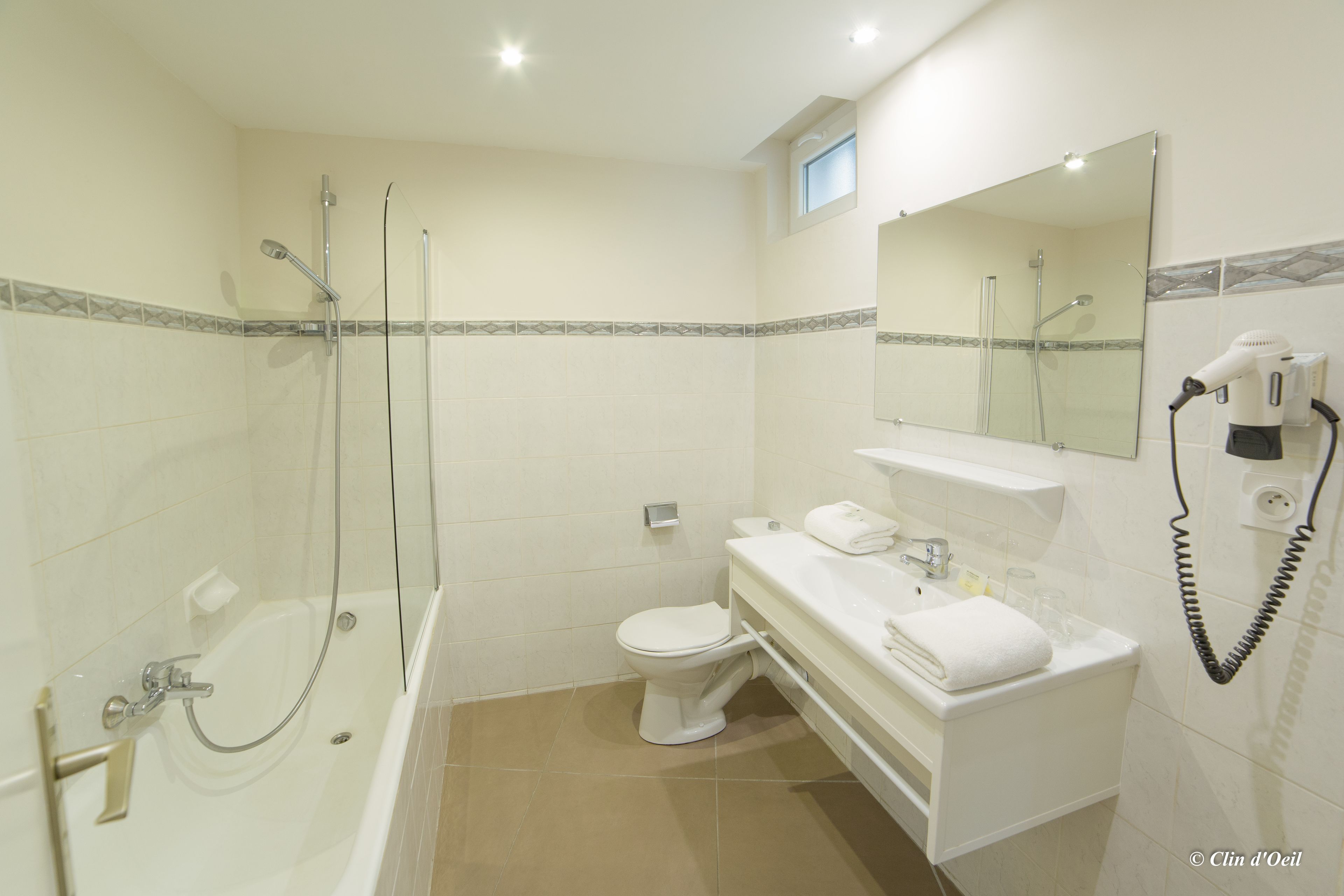 Une salle de bain moderne dotée d’une douche à parois de verre, de toilettes et d’un meuble-lavabo avec un sèche-cheveux.