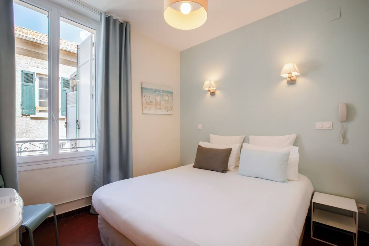 Une chambre d’hôtel avec un lit, une table de chevet, une lampe et une fenêtre avec des rideaux.