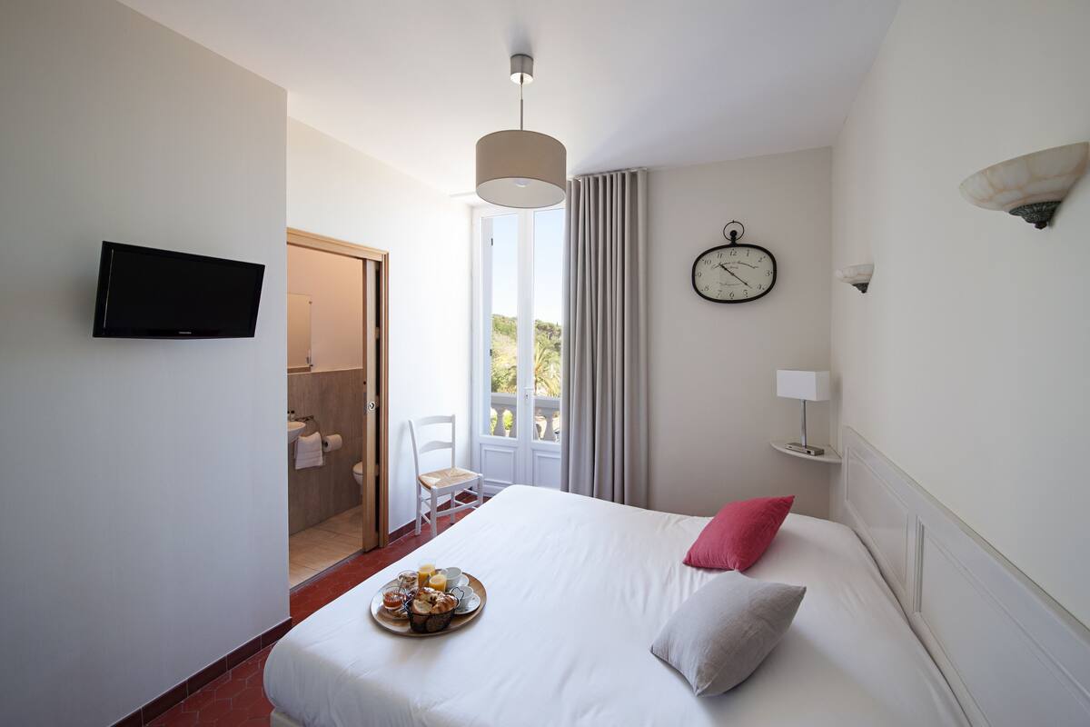 Une chambre d’hôtel avec un lit, une télévision, une horloge et un plateau de petit-déjeuner posé sur le lit.