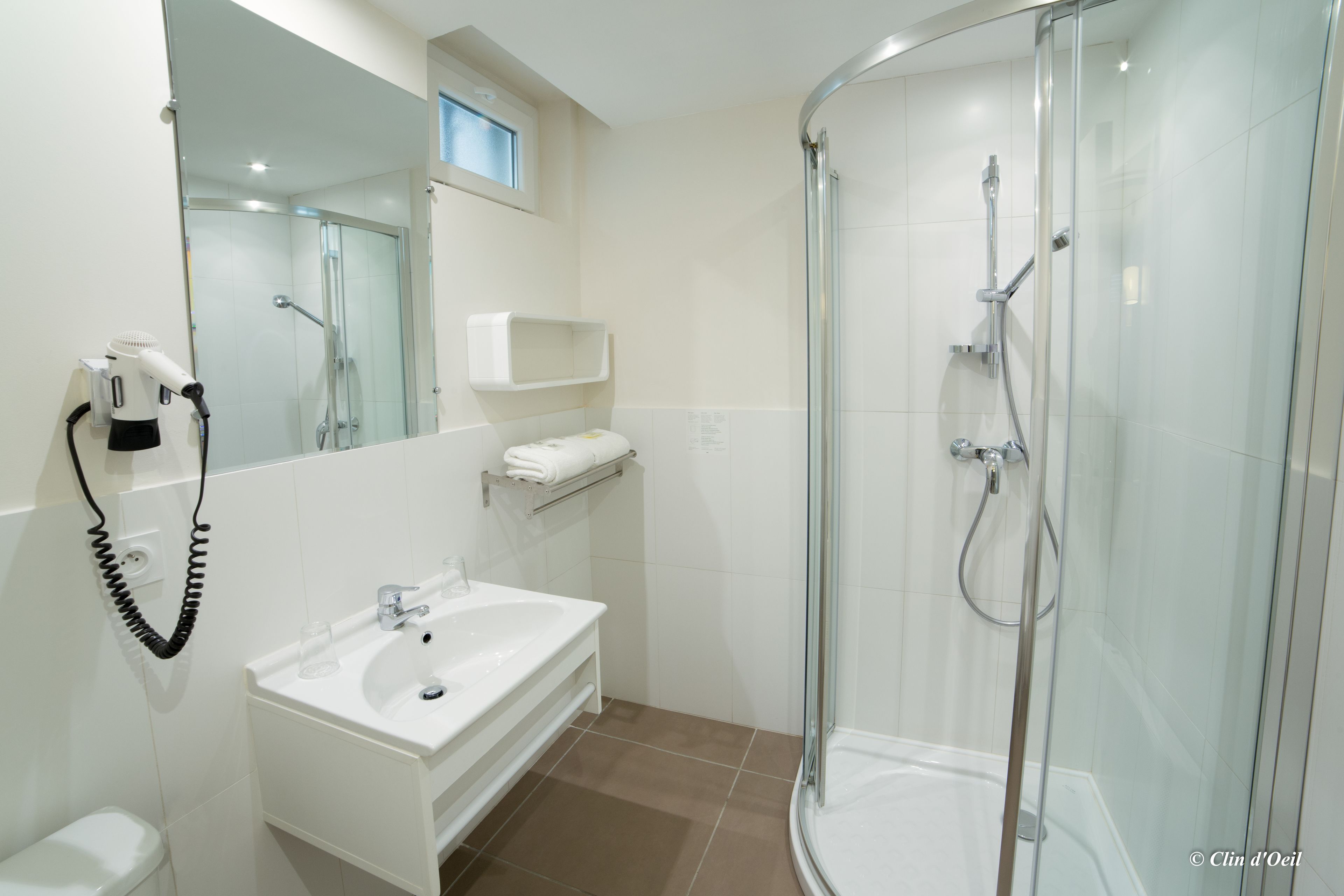 A modern bathroom with a glass-enclosed shower, a white sink, and a hairdryer mounted on the wall.