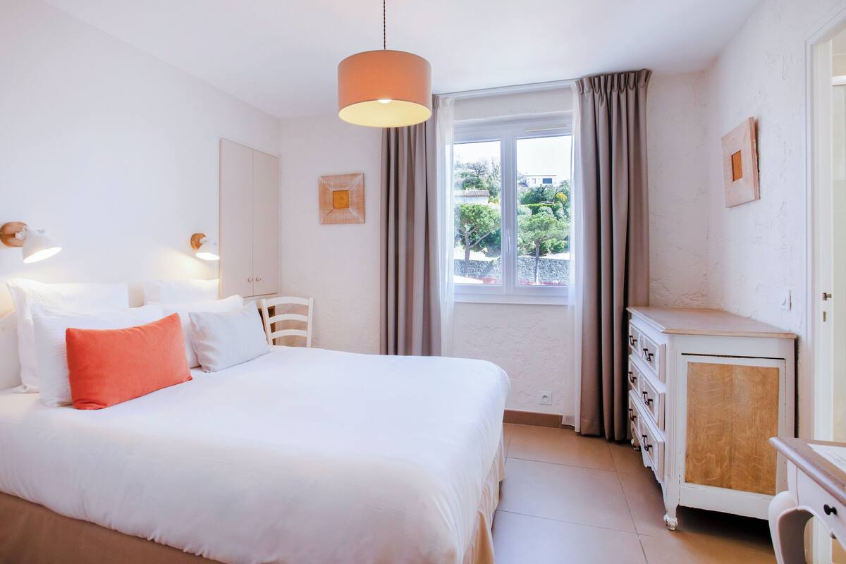 Une chambre à coucher comprenant un lit, une commode, une fenêtre avec des rideaux et des lampes fixées au mur.