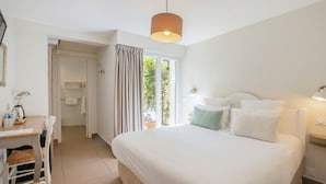 Habitación de hotel con cama, escritorio con silla, lámpara y vistas al exterior con vegetación.