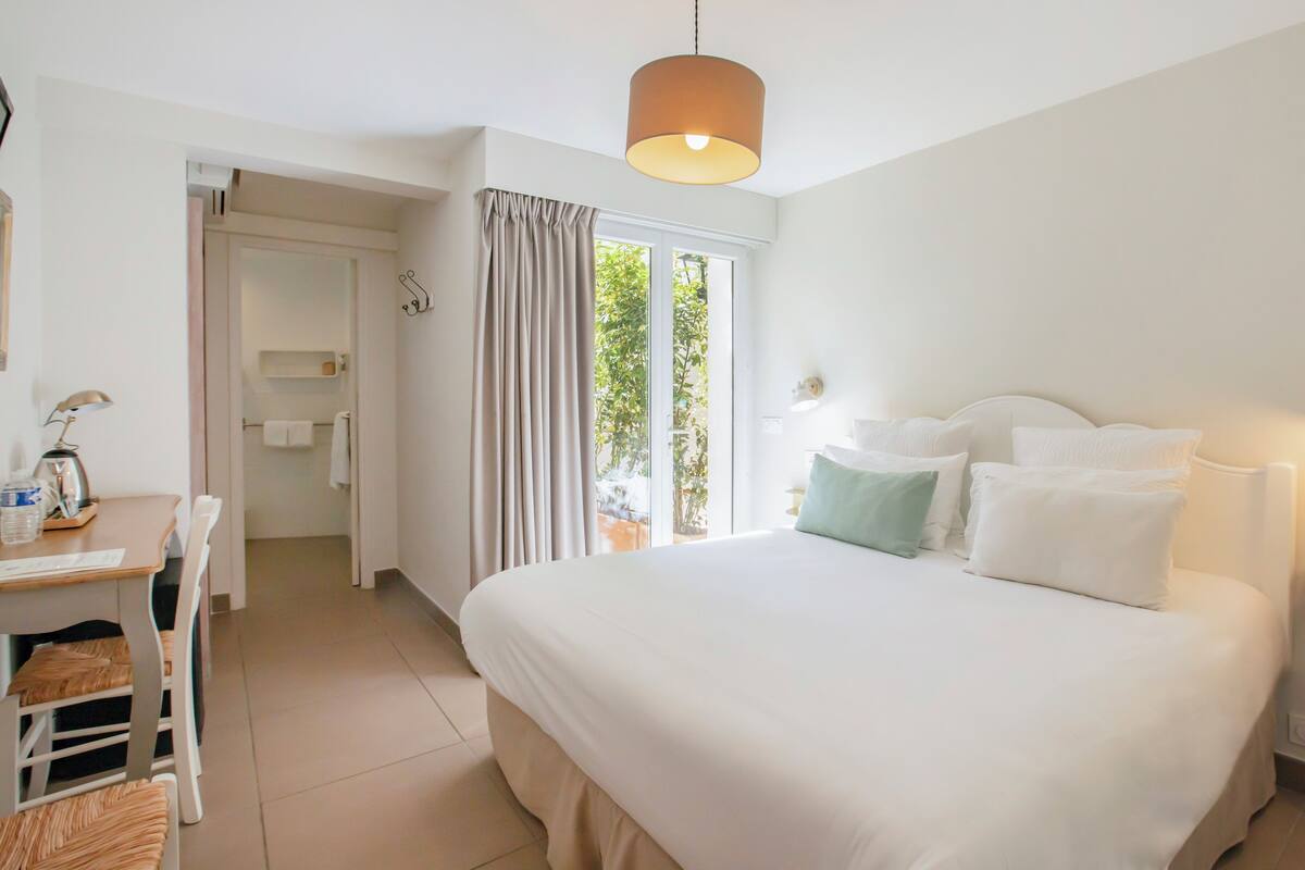 Une chambre d’hôtel avec un lit, un bureau et une chaise, une lampe et une vue sur la verdure.