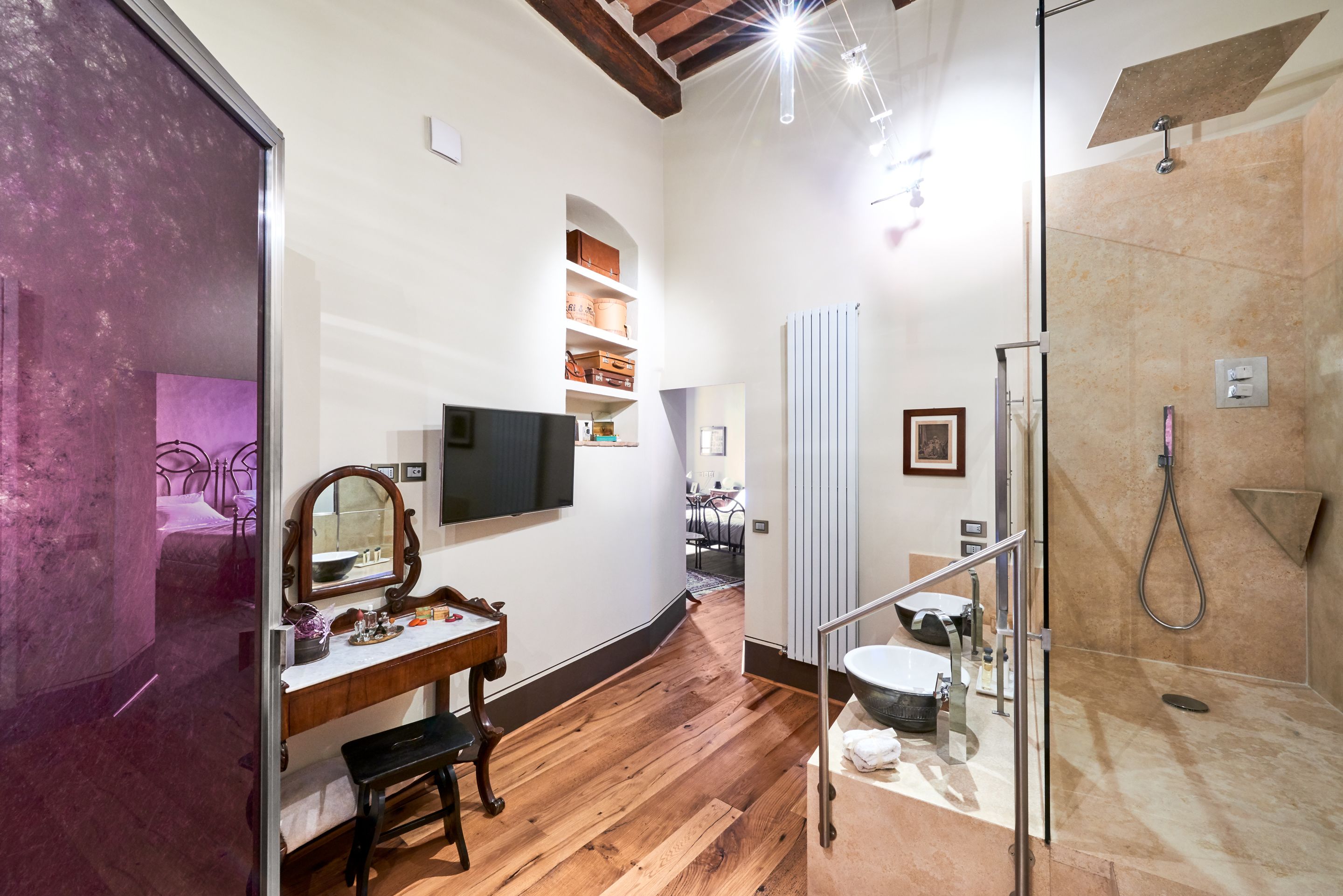 Une salle de bain avec un plancher en bois, une douche en verre, un meuble-lavabo avec un miroir et un téléviseur fixé au mur.
