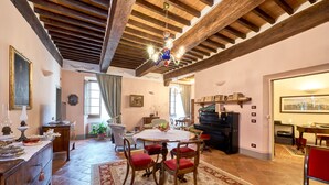 A spacious living room with a wooden ceiling, a dining table with chairs, a piano, and a large window. - Il Tosco (Montepulciano)