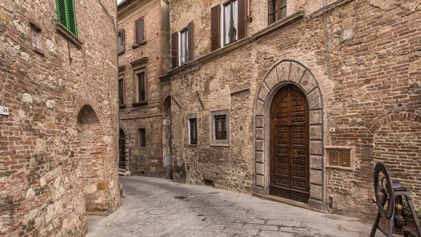 A narrow cobblestone street flanked by historic stone buildings with arched doorways and windows. - Il Tosco (Montepulciano)