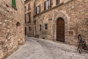 A narrow cobblestone street flanked by historic stone buildings with arched doorways and windows.