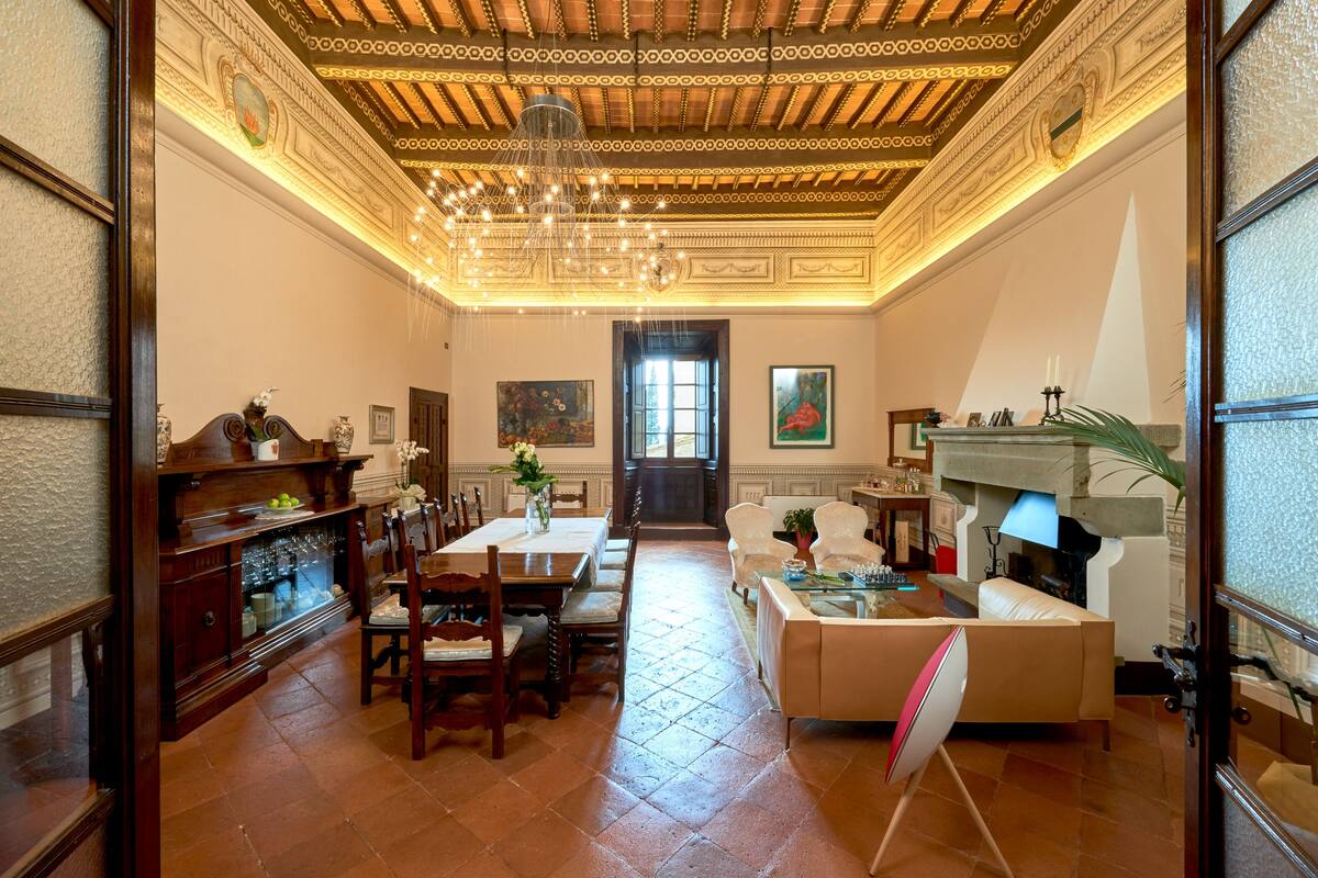 A spacious living room with a dining area, a fireplace, and a chandelier.