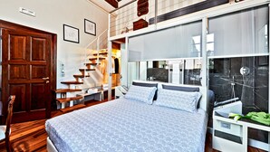 A bedroom with a large bed, wooden flooring, a staircase, and a bathroom with a mirror and sink. - Il Tosco (Montepulciano)