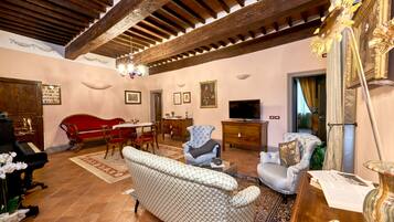A spacious living room with a high ceiling, a grand piano, a red sofa, a patterned sofa, a television, and a dining area with a table and chairs.
