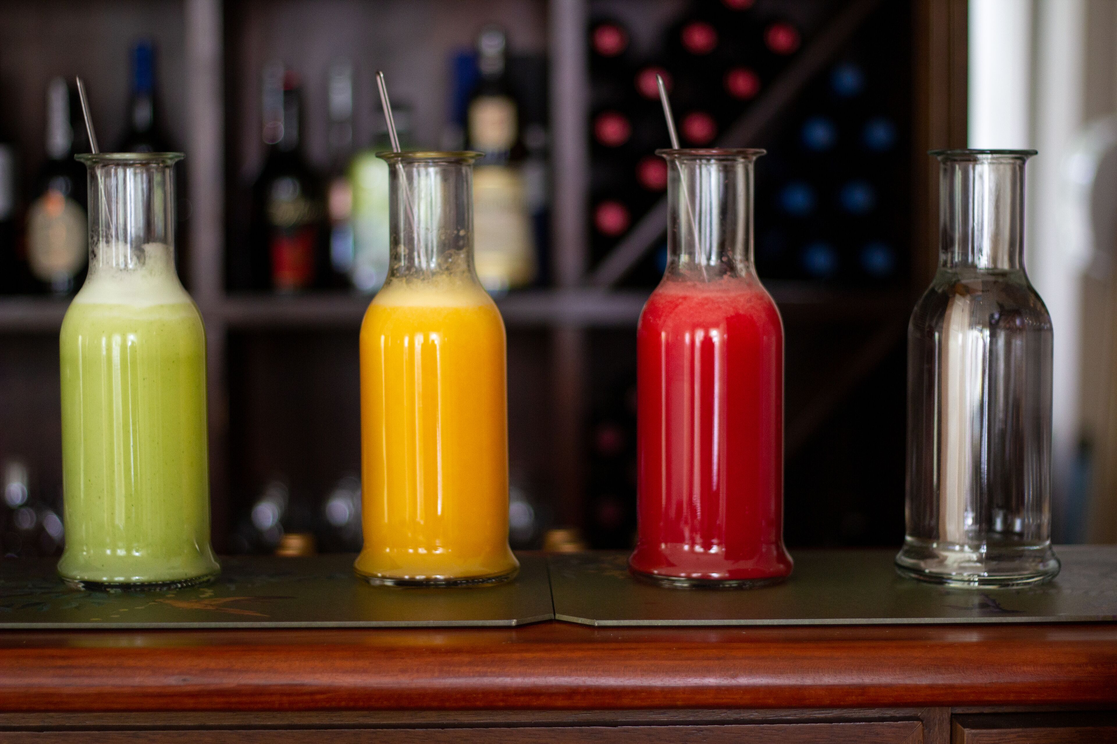 Four glass bottles with different colored liquids on a bar counter.