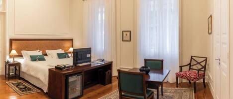A hotel room with a bed, a desk with a television, a chair, a table, and a small cabinet.