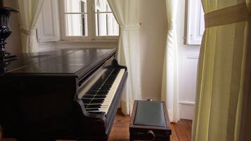 Un piano à queue dans une pièce dont le sol est recouvert de parquet et où sont accrochées des rideaux blancs.
