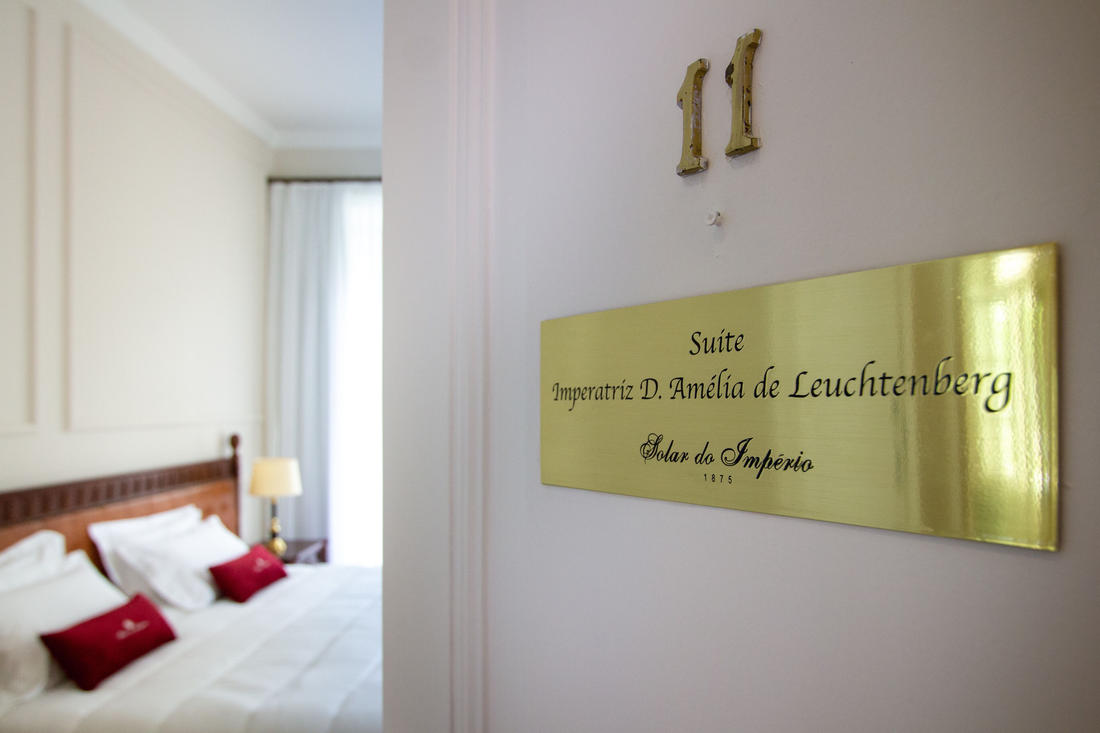 A hotel room with a bed, pillows, and a wall-mounted sign indicating the suite name and address.
