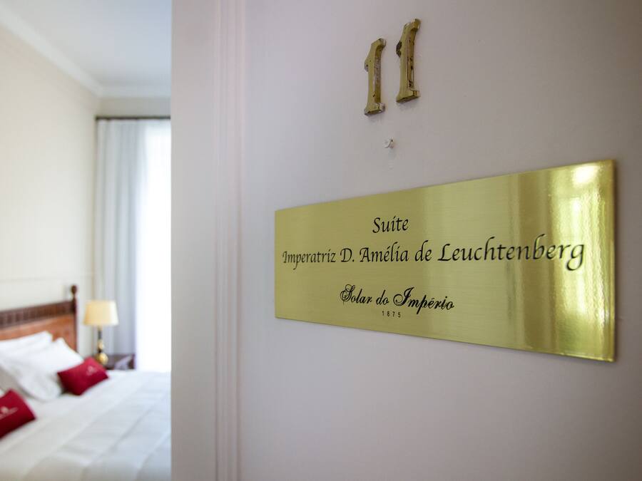 A hotel room with a bed, pillows, and a wall-mounted sign indicating the suite name and address.