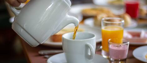 A white teapot pouring coffee into a cup on a saucer.