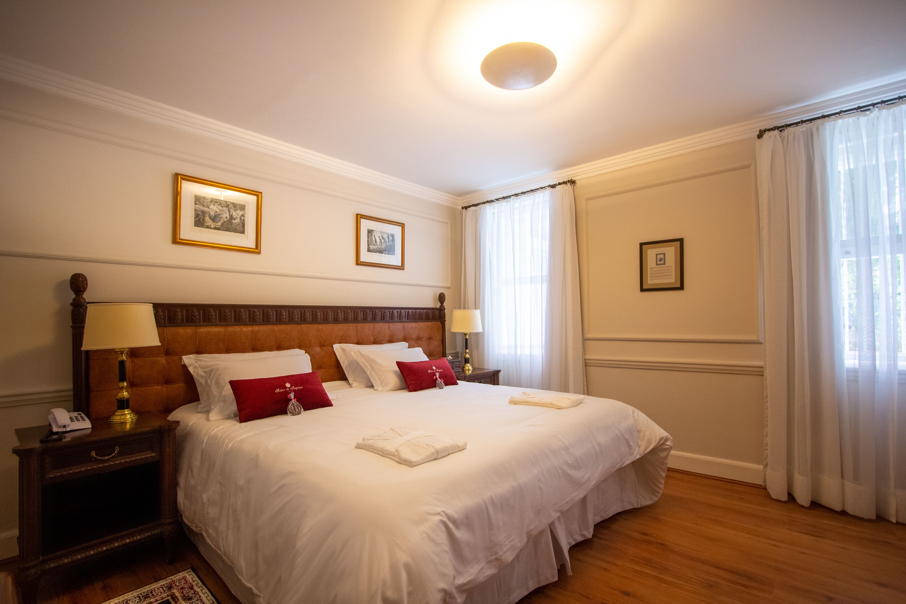 A neatly made bed with white and red bedding, a wooden headboard, and two bedside lamps.