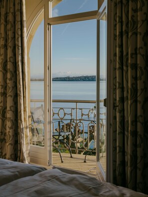 A room with a bed and a balcony with a view of a lake and mountains. - Bad Hotel Überlingen (Ueberlingen)