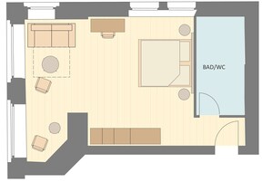 Planta baixa de um quarto de hotel com uma cama, um sofá, uma mesa pequena e uma área de estar circular. O quarto possui um banheiro e um vaso sanitário.