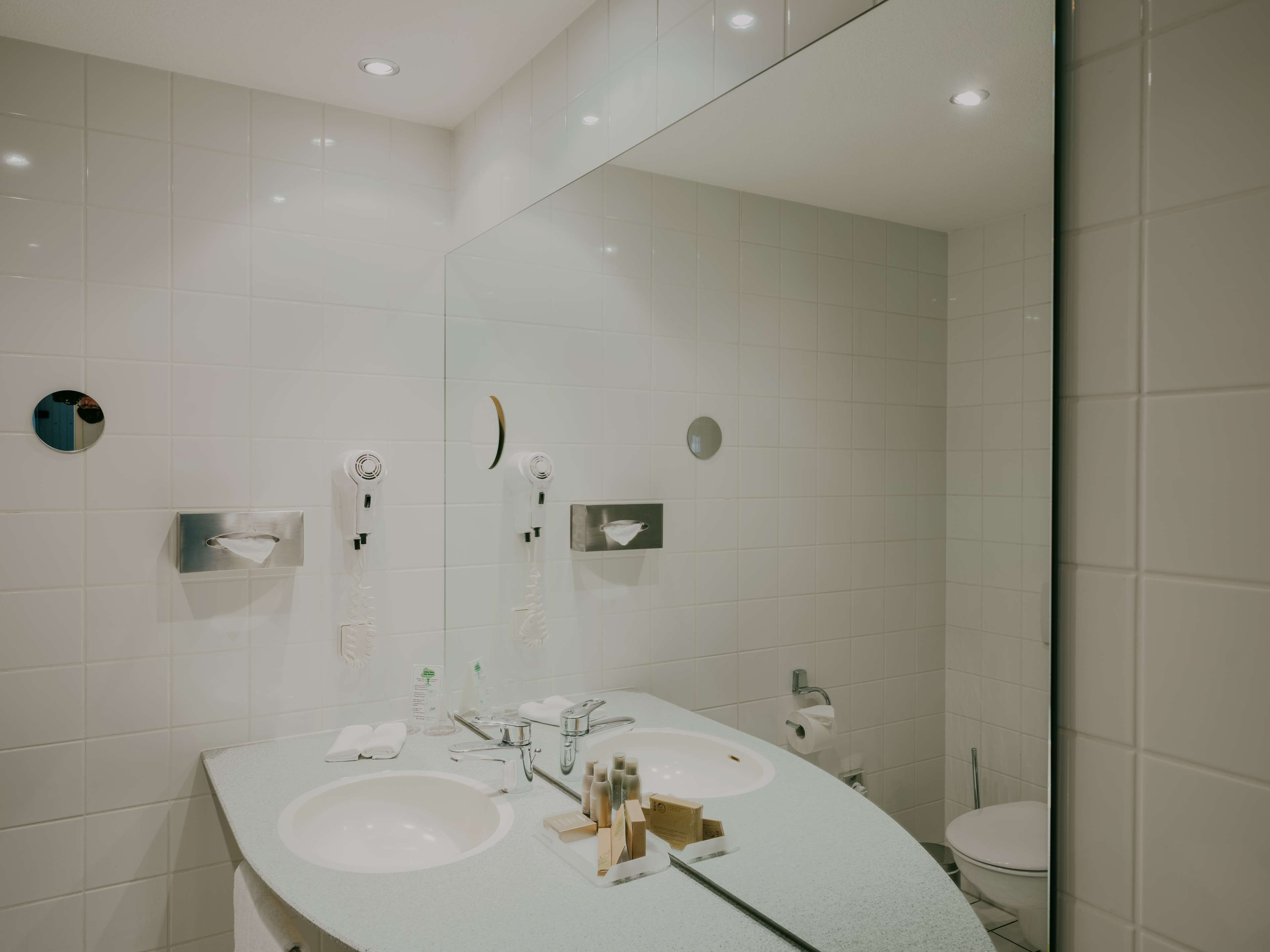 A modern bathroom with two sinks, a mirror, and a toilet.