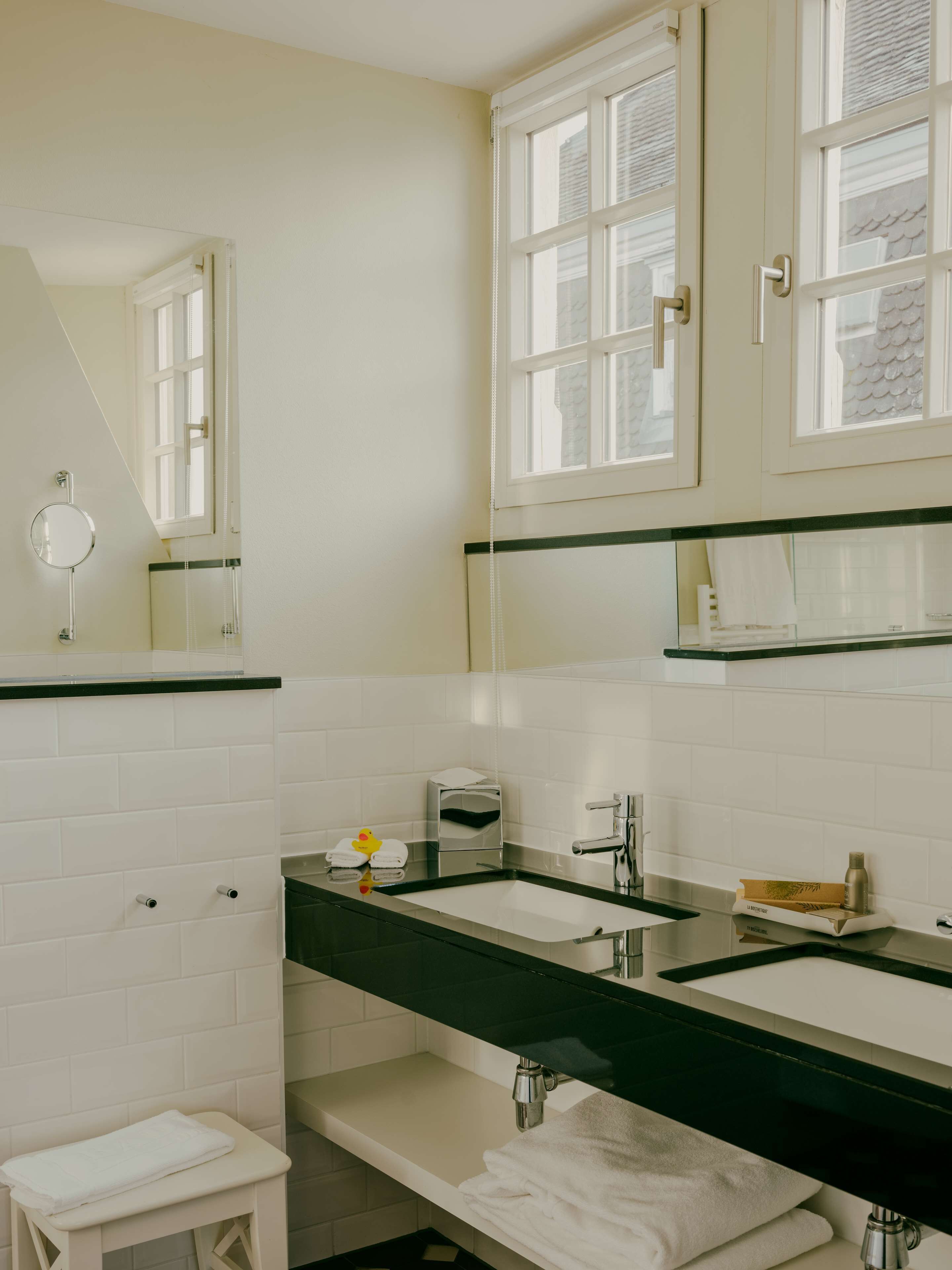A modern bathroom with two sinks, a mirror, a towel rack, and a window.