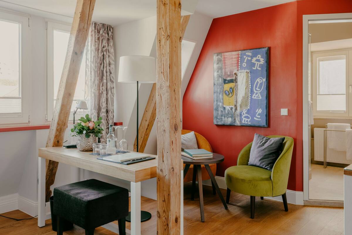 A modern room with a wooden ceiling, a red accent wall, a green chair, a white desk, and a floor lamp.